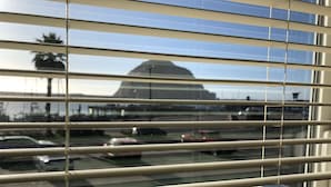 A view through window blinds of a parking lot with several cars and a large building in the background.