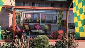 A covered outdoor seating area with red and purple chairs, a glass table, and various plants.