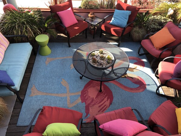 Un espace patio agrémenté de plusieurs chaises rouges, d’une table ronde ornée d’un cactus et d’un tapis coloré à motifs de feuilles.