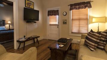 A living room with a television, a door, a window with blinds, a sofa, and a coffee table.