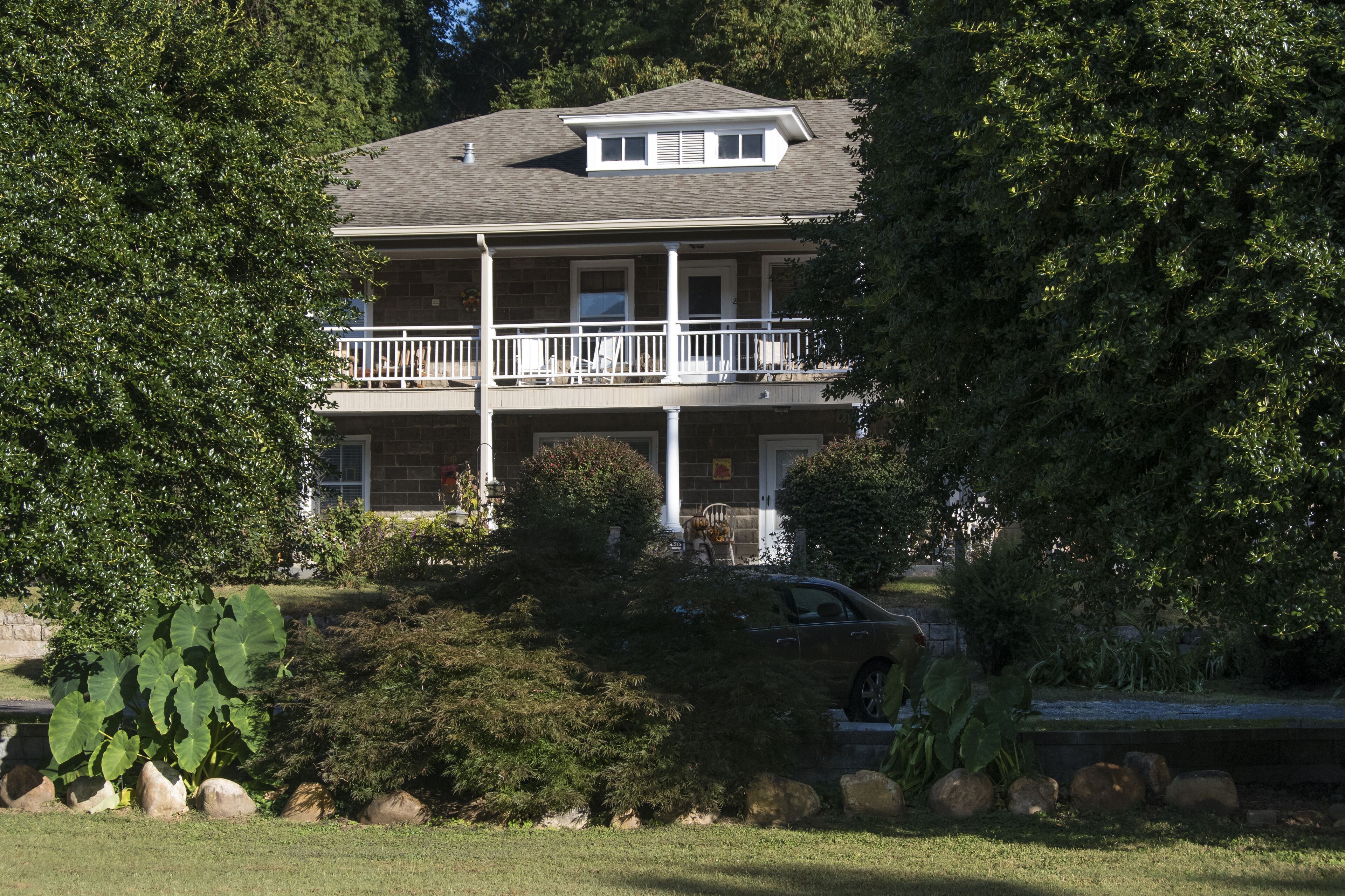 A two-story house with a balcony, surrounded by trees and a cactus.
