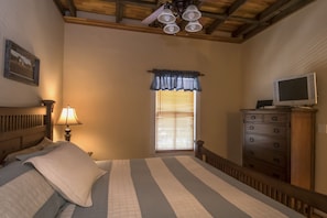 A bedroom with a bed, a dresser, a television, a window with blinds, and a ceiling fan. - Calhoun House Inn & Suites (Bryson City)