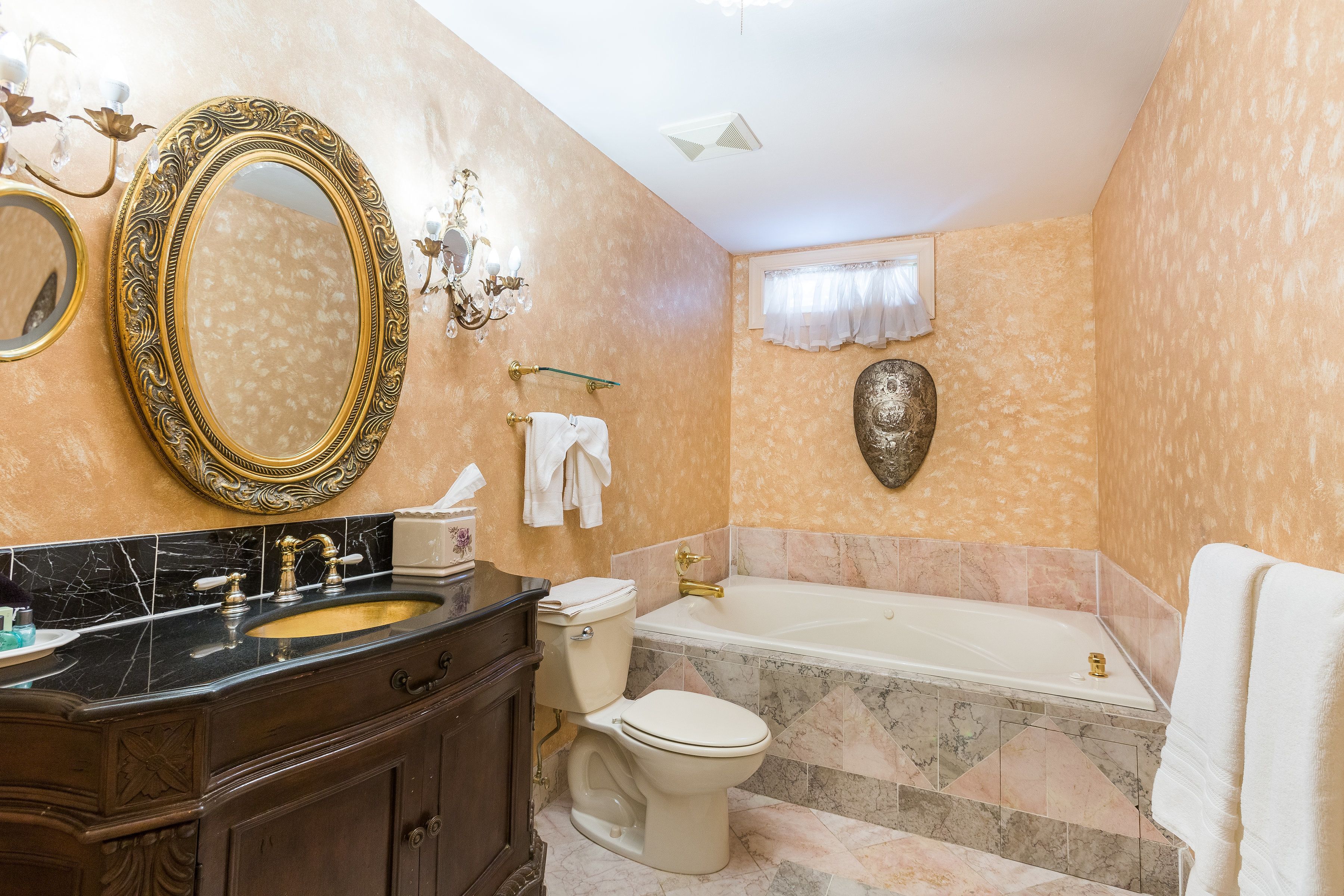 A bathroom with a large oval mirror, a bathtub, a toilet, and a sink with a marble countertop.