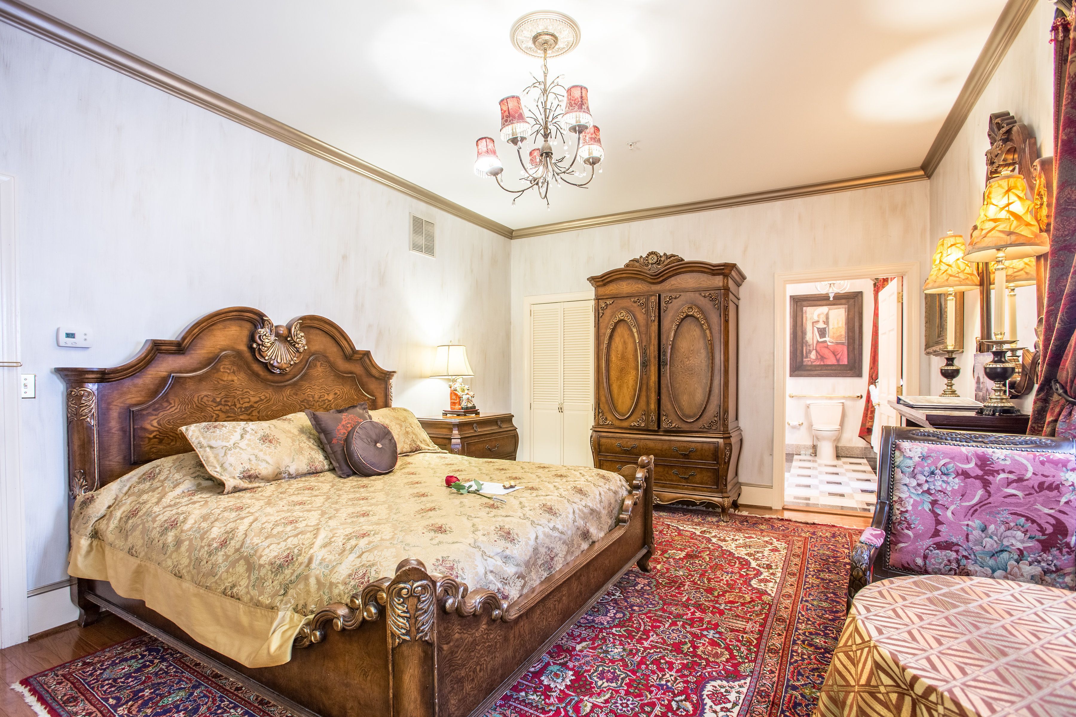 Ein geräumiges Schlafzimmer mit einem großen Holzbett, einem klassischen Kronleuchter und einem traditionellen Holzschrank.