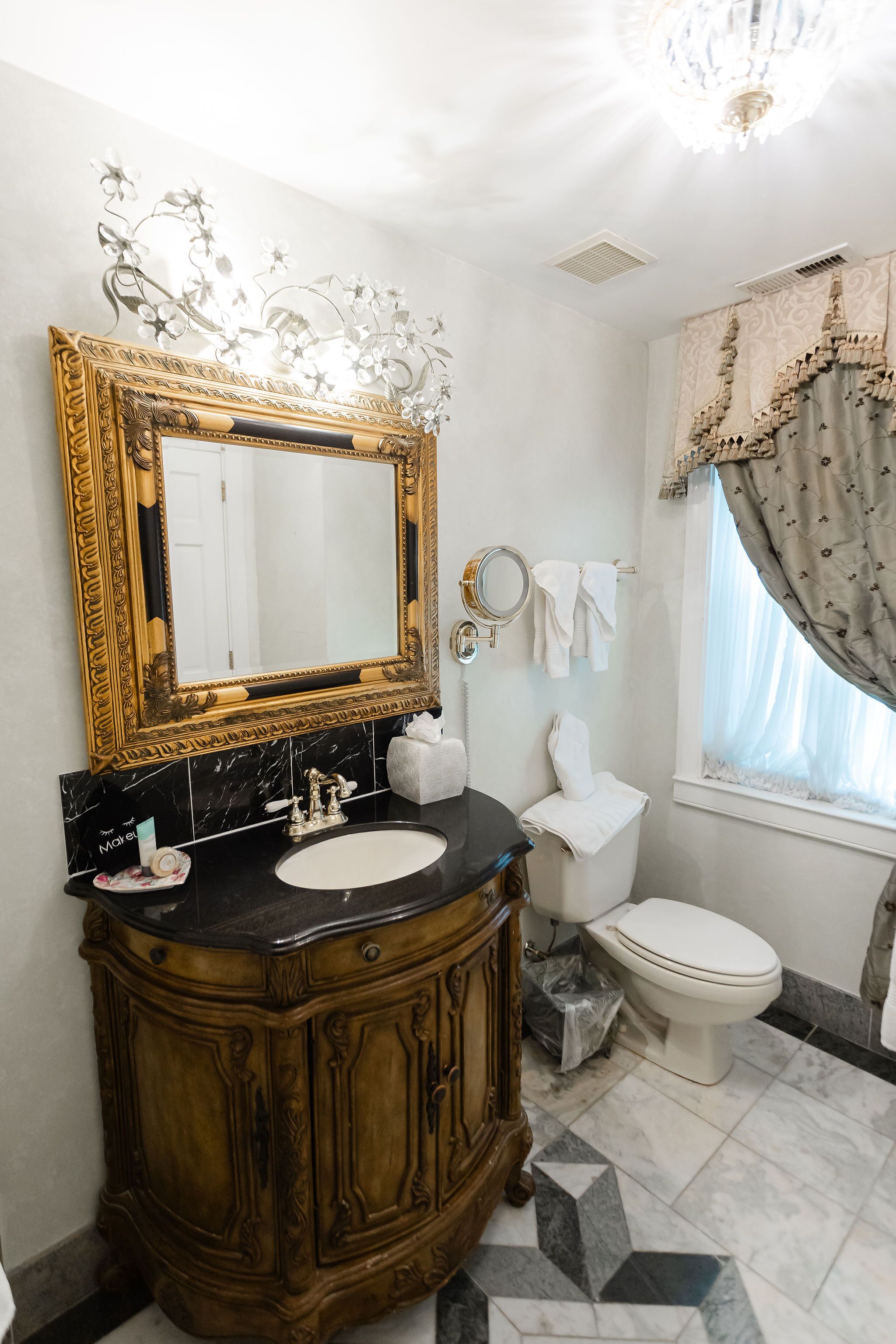 A bathroom with a large ornate mirror, a black marble sink, a wooden vanity, and a white toilet.