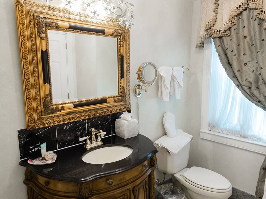 A bathroom with a large ornate mirror, a black marble sink, a wooden vanity, and a white toilet.