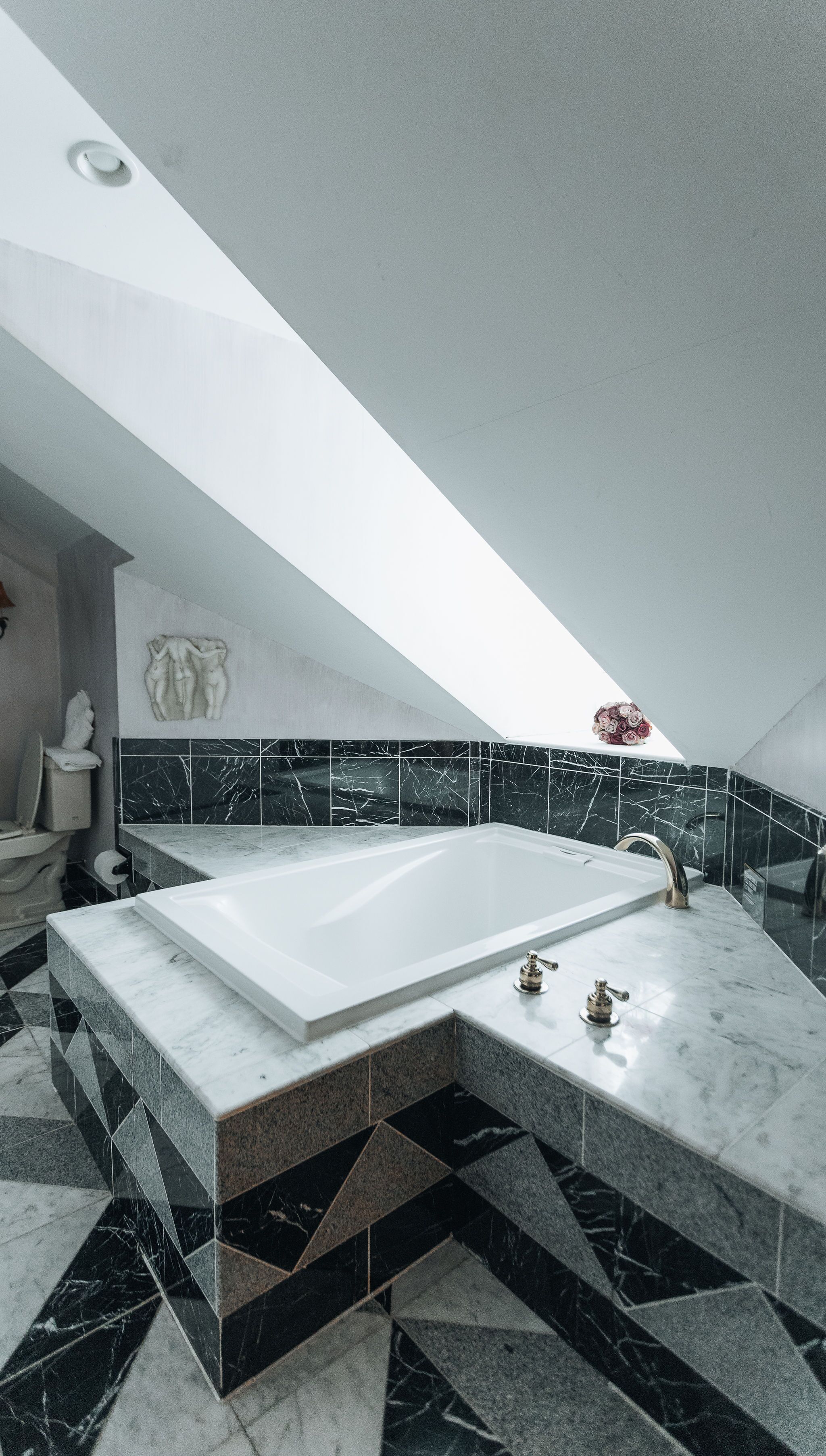 A modern bathroom with a freestanding bathtub, black and white marble tiles, and a skylight.