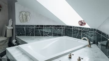 A modern bathroom with a freestanding bathtub, black and white marble tiles, and a skylight.