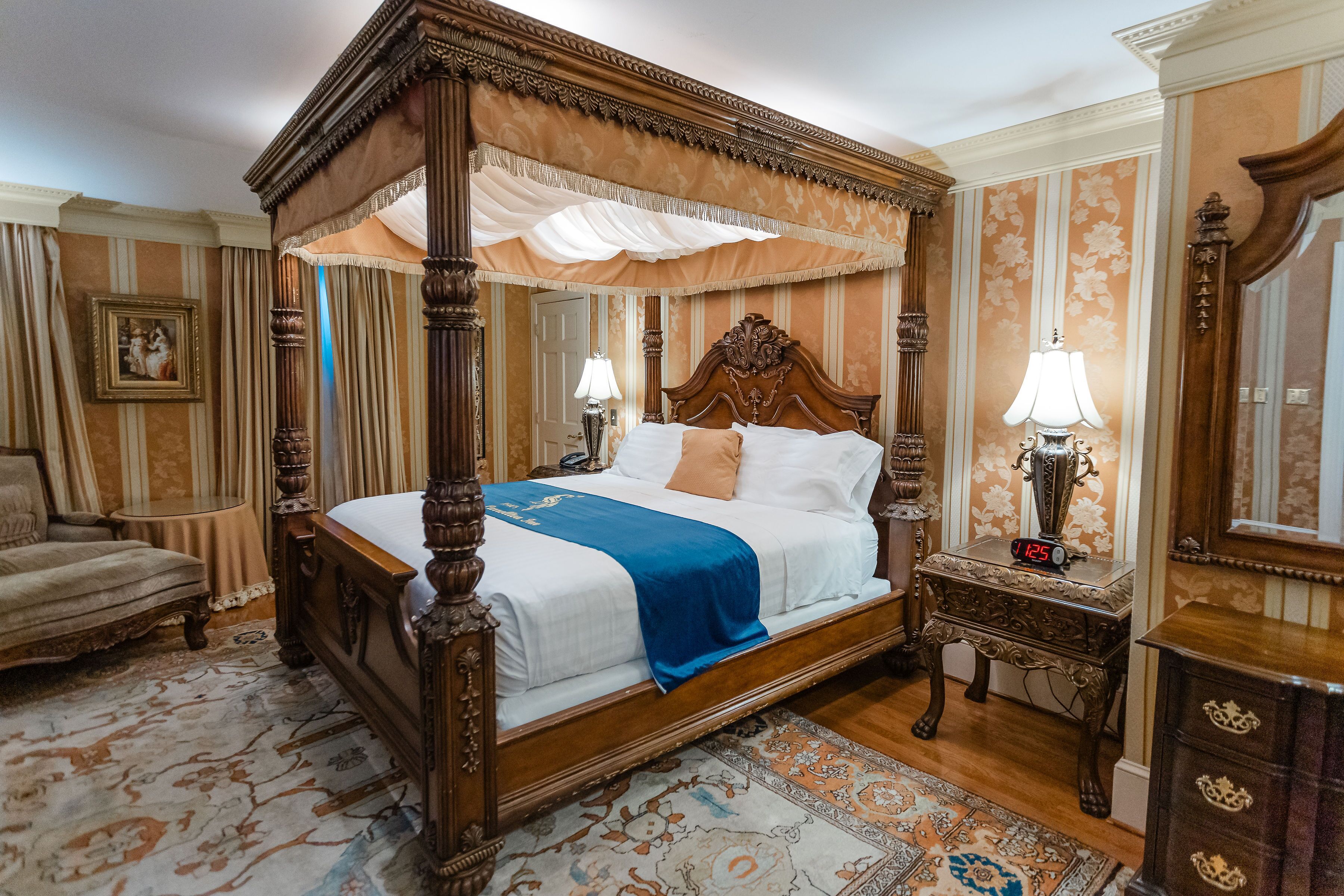 A four-poster bed with a canopy, a nightstand with a clock, a chair, and a mirror.
