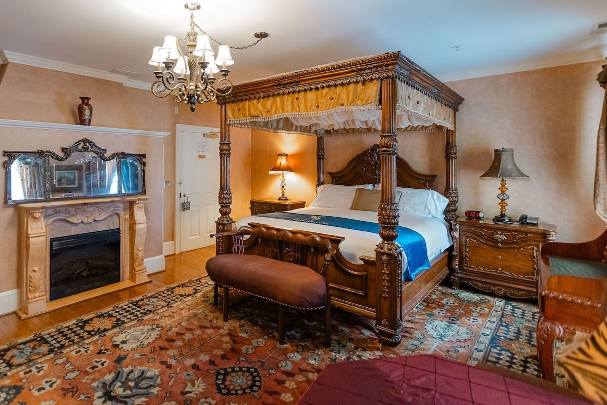A four-poster canopy bed with a wooden finish, a chandelier, and a patterned rug.