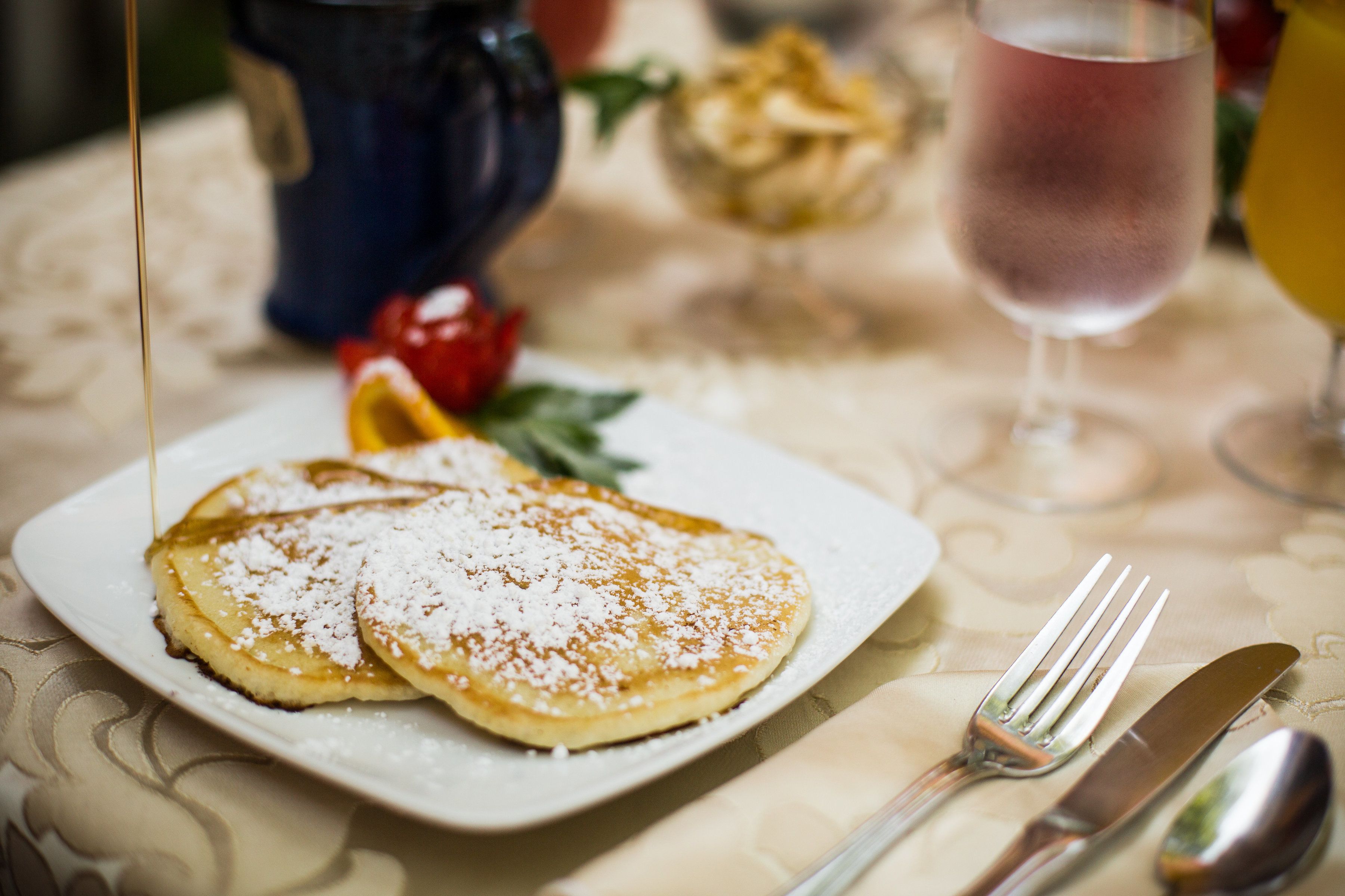 Une assiette de crêpes nappées de sirop et saupoudrées de sucre glace, une fourchette et un couteau, le tout posé sur une table recouverte d’une nappe à motifs.
