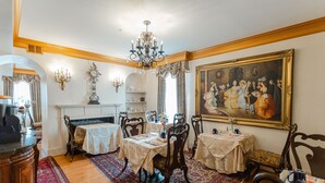 Un menjador amb un penjador, cadires ornamentades, un quadre gran i una llar de foc.
