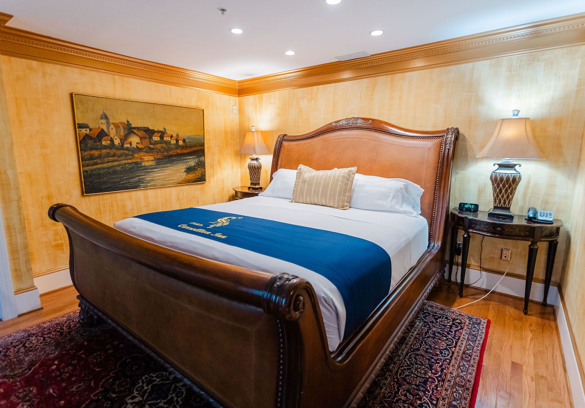 Un grand lit avec une tête de lit en bois, une couvre-lit bleue et blanche, deux lampes de chevet, un tableau au mur et un plancher en bois.