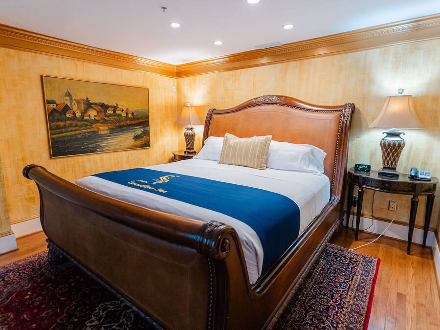 Un grand lit avec une tête de lit en bois, une couvre-lit bleue et blanche, deux lampes de chevet, un tableau au mur et un plancher en bois.