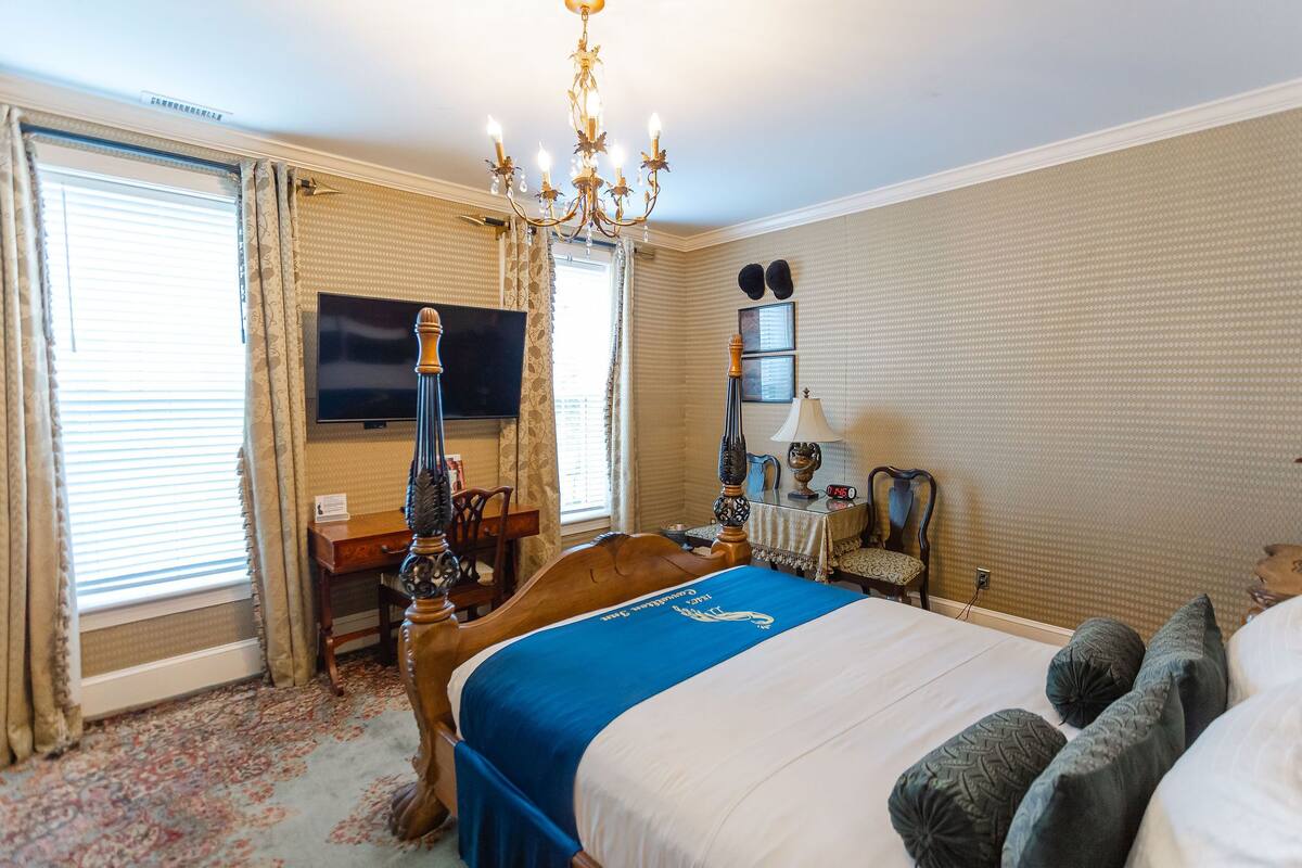 A hotel room with a large bed, a desk with a computer, a television, and a chandelier.