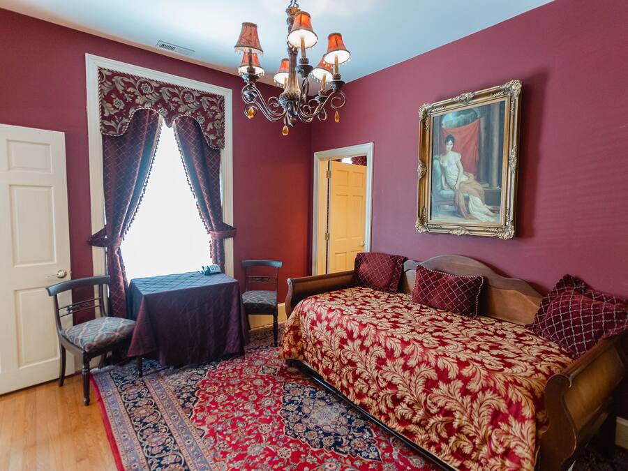A bedroom with a large bed, a chandelier, a painting, and a window with curtains.