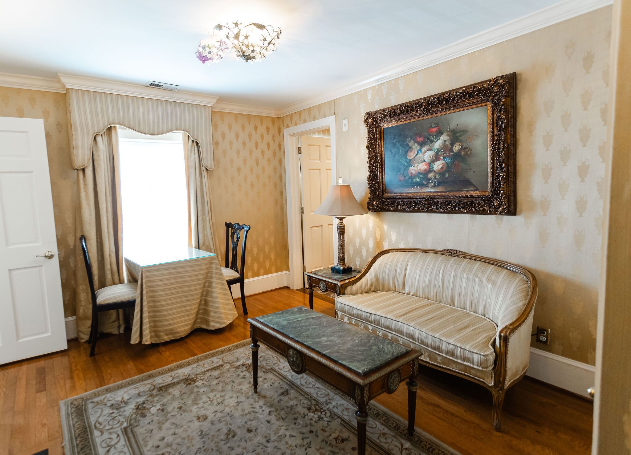 A room with a sofa, a table, a chair, a lamp, and a painting on the wall.
