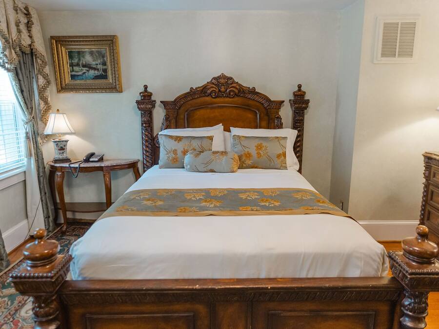 A neatly made bed with floral bedding, a wooden headboard, and a bedside table with a lamp.