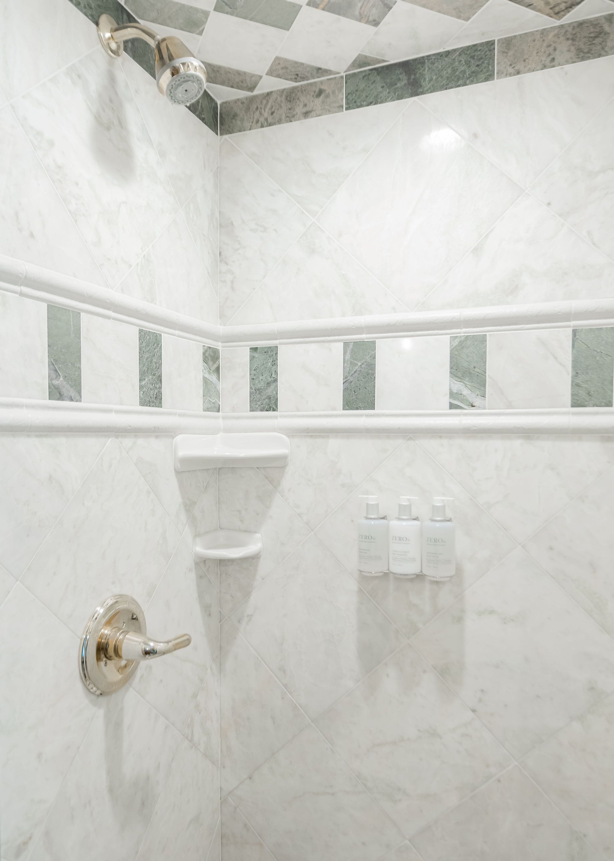 Casa de banho com chuveiro, azulejos de mármore branco e uma prateleira com artigos de higiene pessoal.