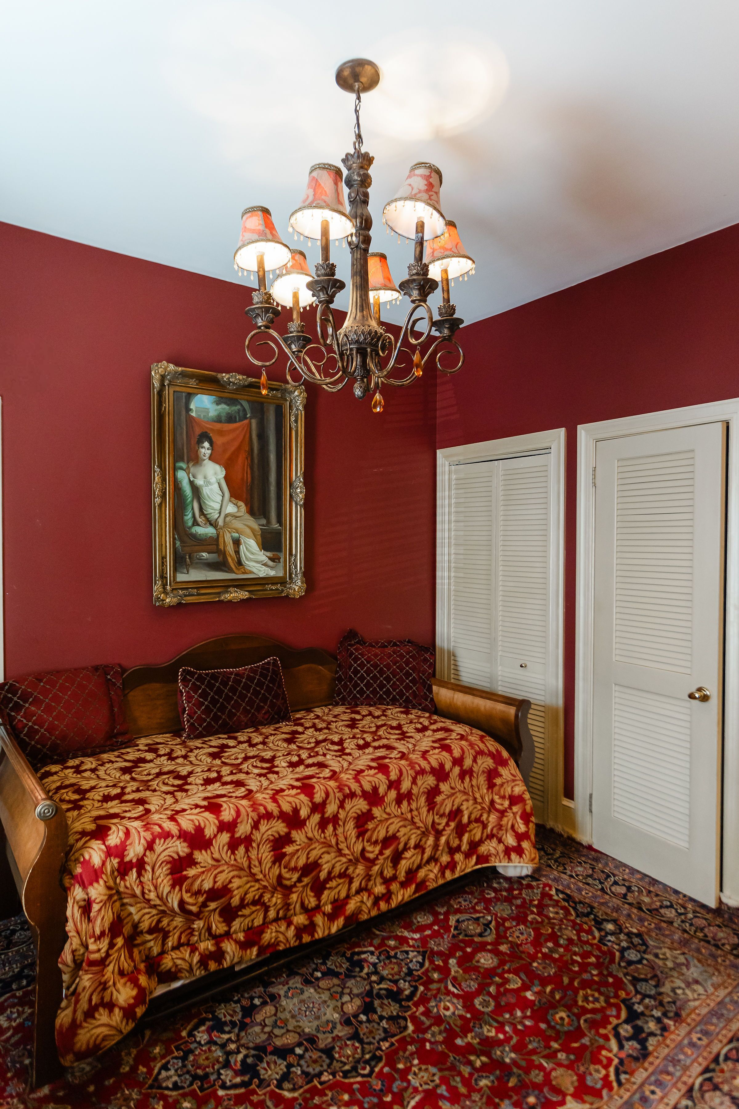 A bedroom with a bed, a chandelier, a framed painting, and a patterned rug.
