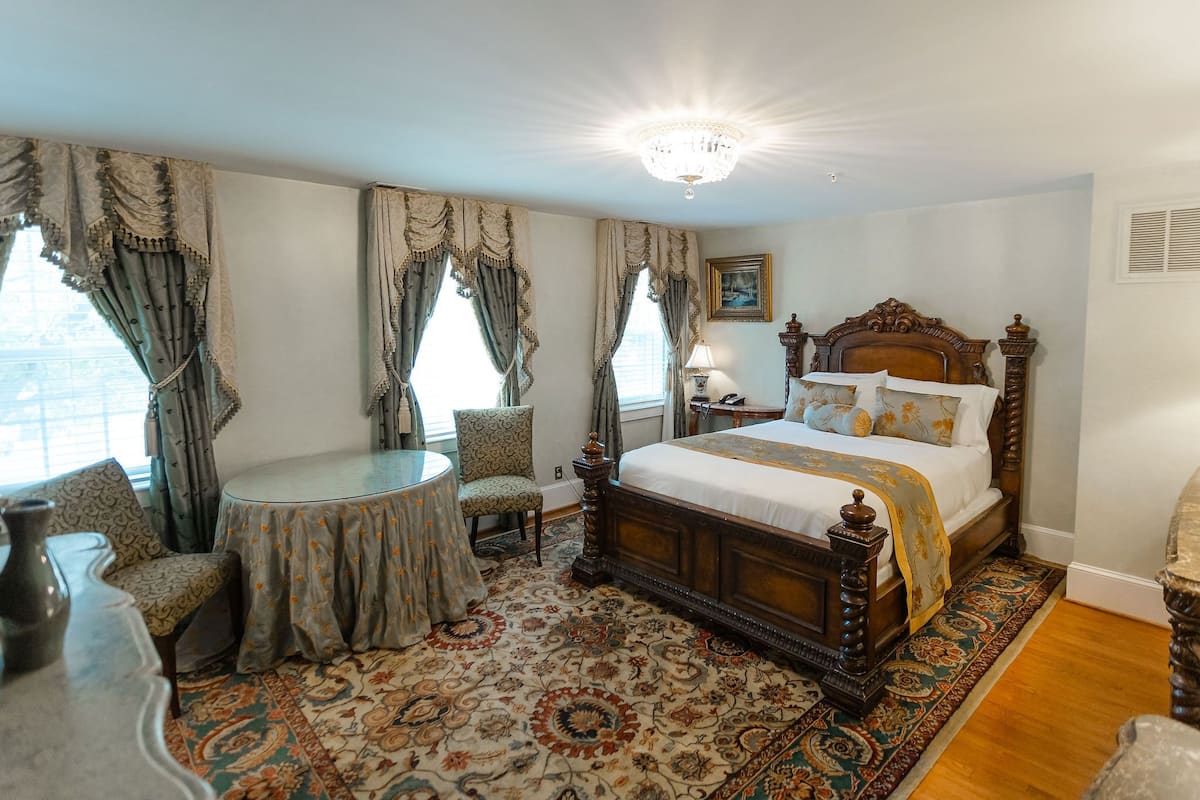 A traditional bedroom with a large bed, a round table, and a patterned carpet.