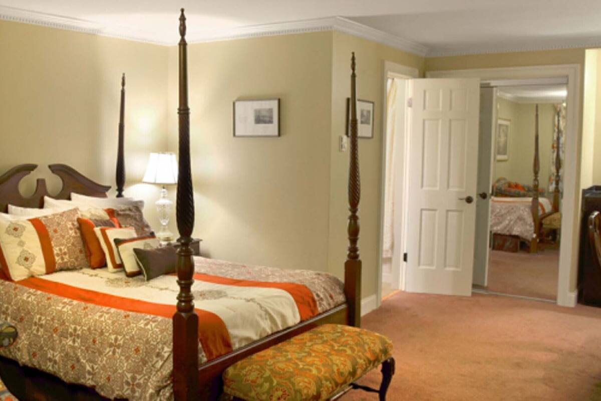 A four-poster bed with a wooden headboard, a bedside table with a lamp, and a colorful sofa with a red cushion.