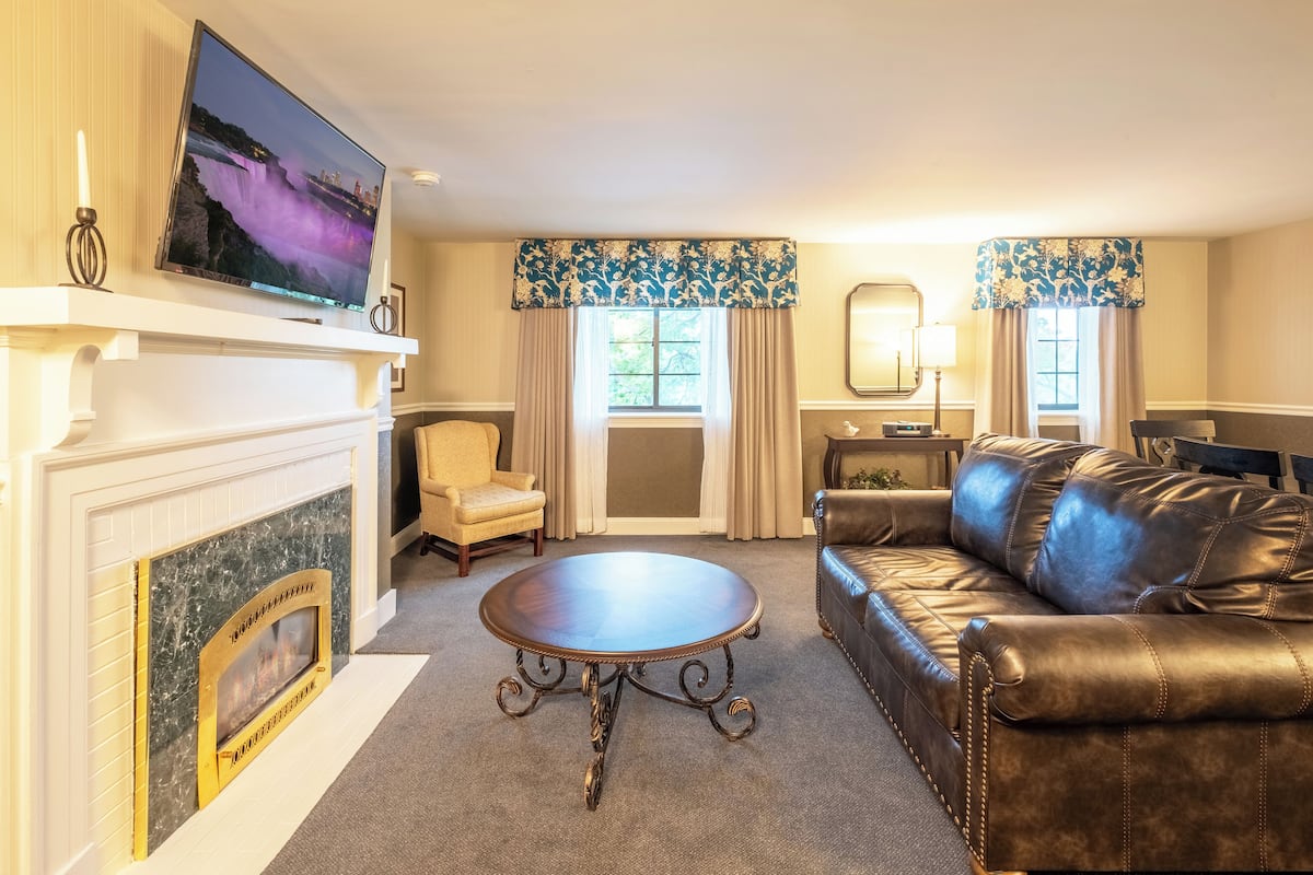 A living room with a fireplace, a television mounted above it, a leather sofa, and a round coffee table.