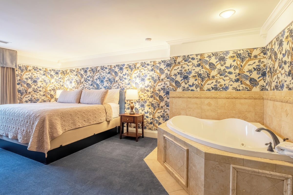 A bedroom with a large bed, a nightstand, a lamp, and a bathtub.