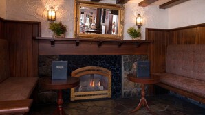 A cozy corner with a stone fireplace, two wooden tables, and a bench. - Red Coach Inn (Niagara Falls)