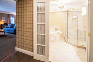 A hotel room with a living area featuring a blue sofa and a small table, a bathroom with a glass shower enclosure, and a checkered wall pattern. - Red Coach Inn (Niagara Falls)