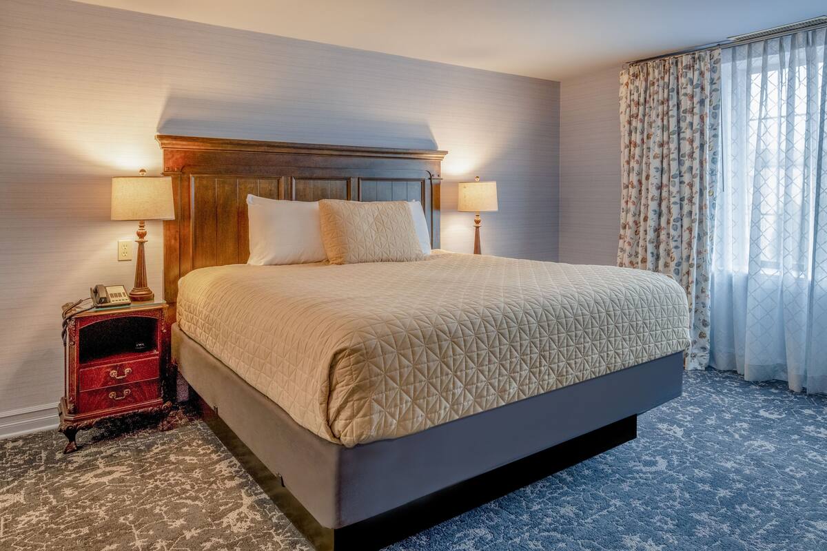 A large bed with a quilted headboard, two bedside lamps, a telephone, and a red nightstand with drawers.