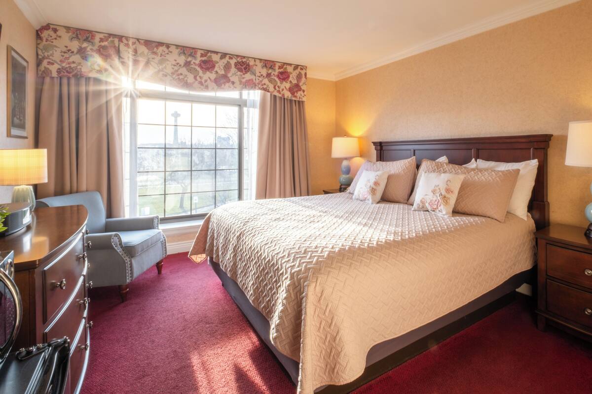 A hotel room with a large bed, a dresser, a chair, and a window with curtains.