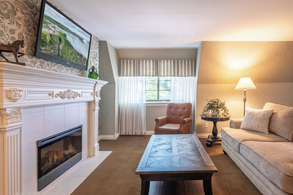 A living room with a fireplace, a television mounted above it, a sofa, a coffee table, and a lamp.