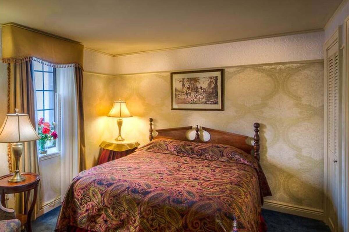 A hotel room with a bed, a chair, a lamp, and a window with curtains.