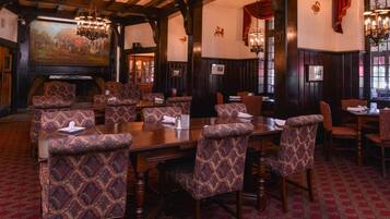 A dining area with patterned upholstered chairs, wooden tables, and a large painting on the wall.