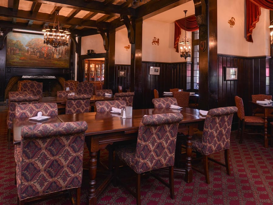 A dining area with patterned upholstered chairs, wooden tables, and a large painting on the wall.
