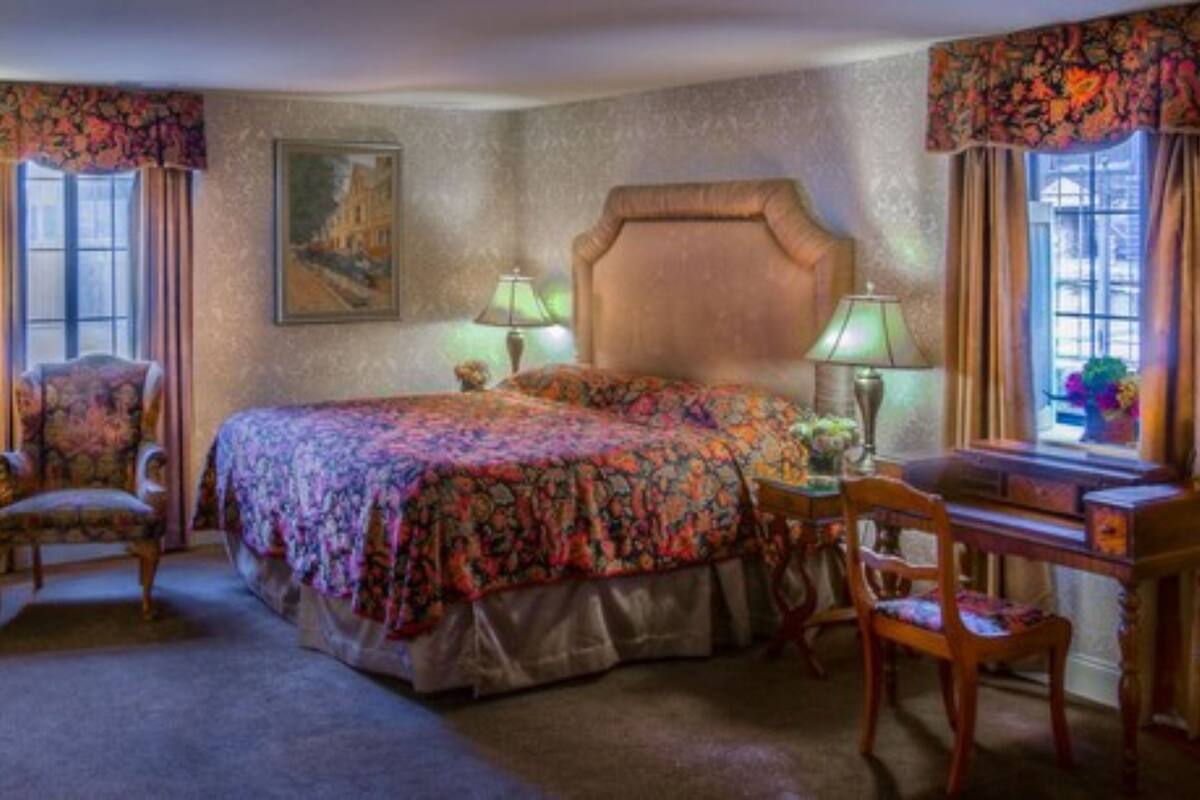 A bedroom with a large bed, two bedside lamps, a chair, a desk, and a window with curtains.