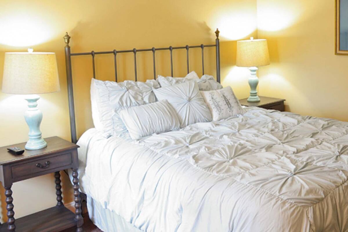 A neatly made bed with white bedding, two bedside tables with lamps, and a framed picture on the wall.