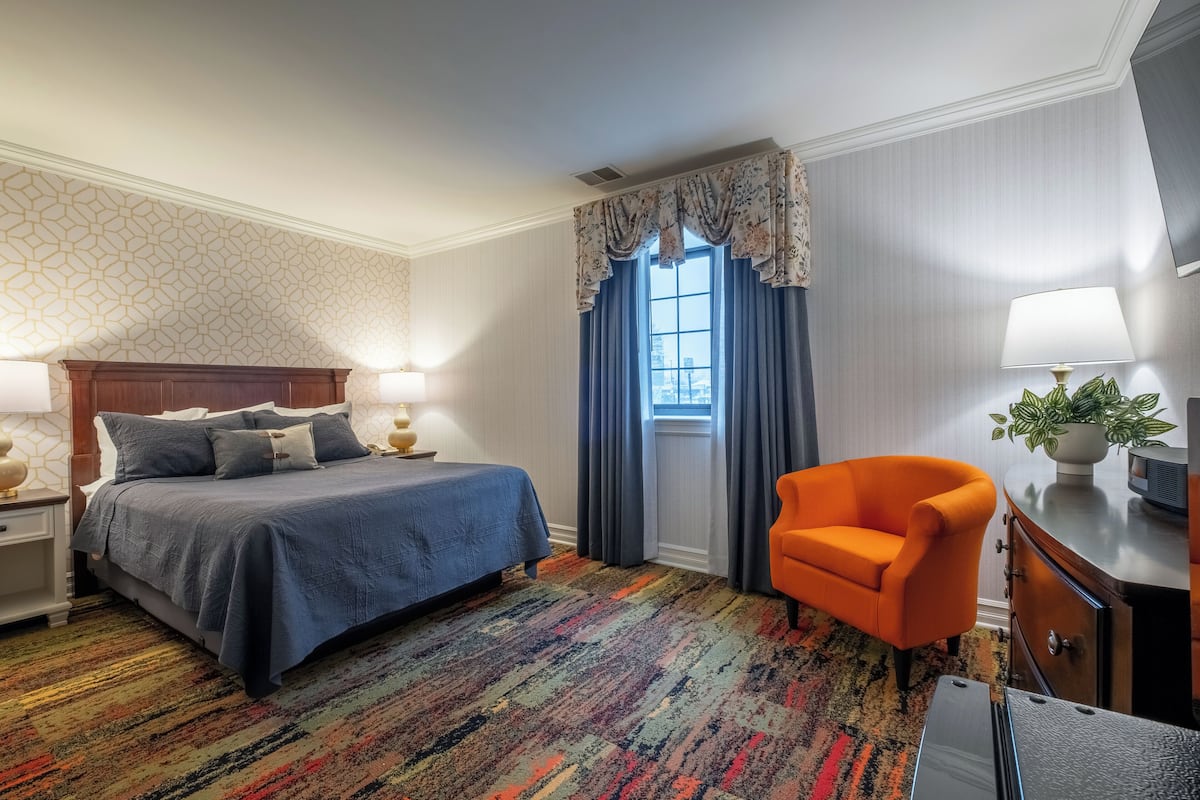 A hotel room with a bed, a chair, a desk, a lamp, and a window with curtains.