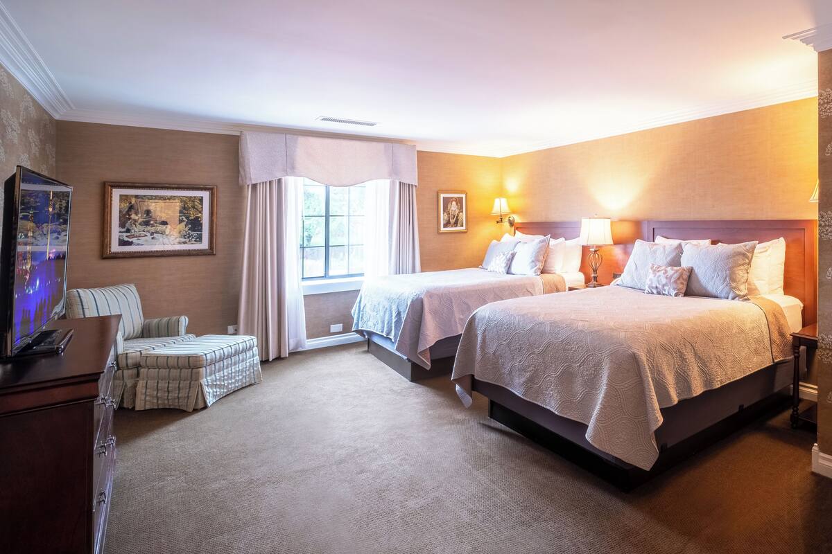 A hotel room with two beds, a sofa, a TV, and artwork on the walls.