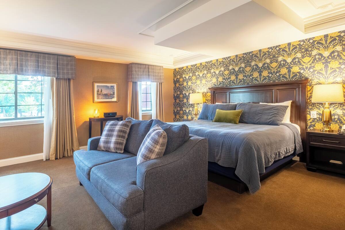 A hotel room with a large bed, a sofa, a small table, and a nightstand with lamps.