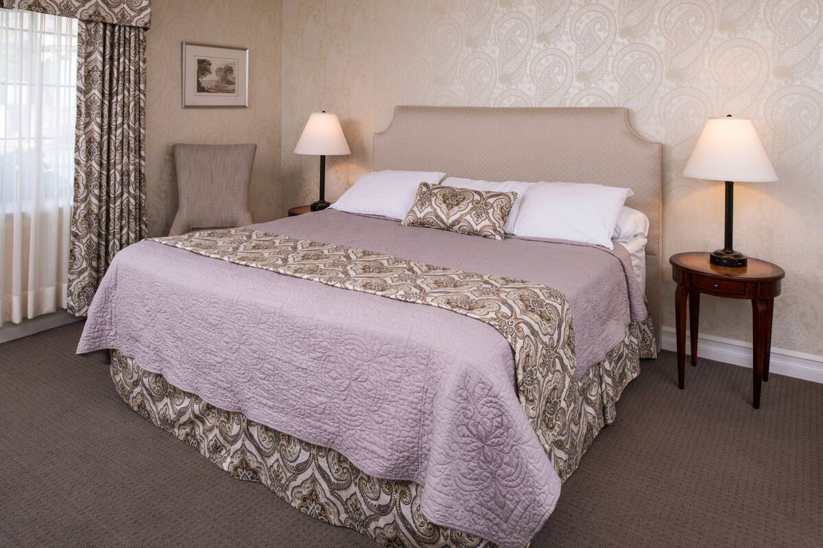 A neatly made bed with a patterned bedspread, two bedside lamps, and a framed picture on the wall.