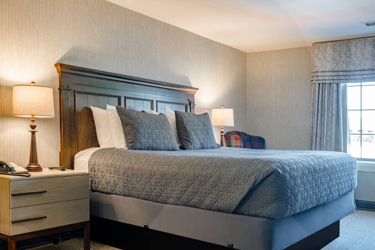 A neatly made bed with a quilted cover, a wooden headboard, and two bedside lamps.