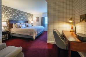 A hotel room with a large bed, a desk with a lamp, and a chair. - Red Coach Inn (Niagara Falls)