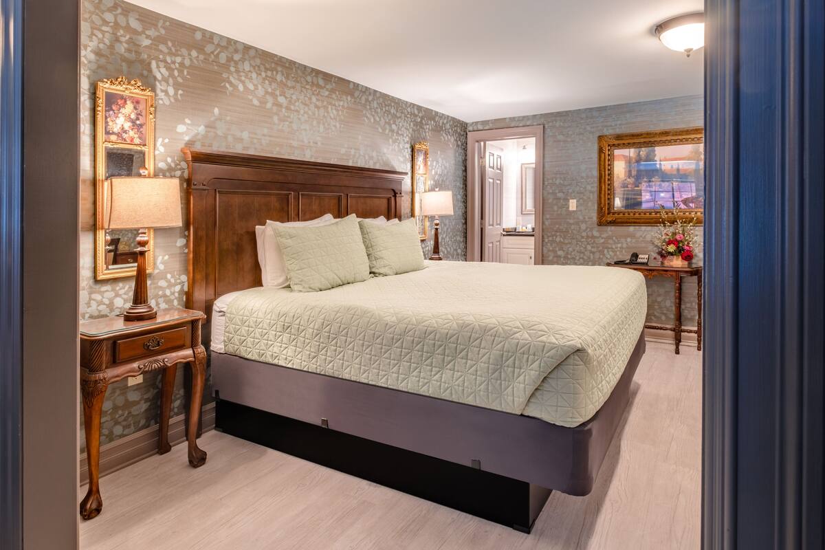 A bedroom with a large bed, wooden headboard, two bedside tables with lamps, and a mirror.