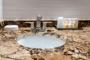 A bathroom with a granite countertop, a sink, and toiletries.