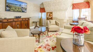 A living room with a sofa, armchairs, a coffee table, and a TV mounted on the wall.