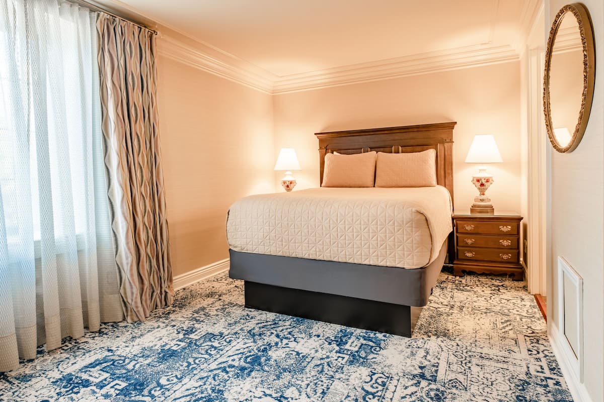 A hotel room with a bed, two bedside lamps, a dresser, a mirror, and a patterned carpet.