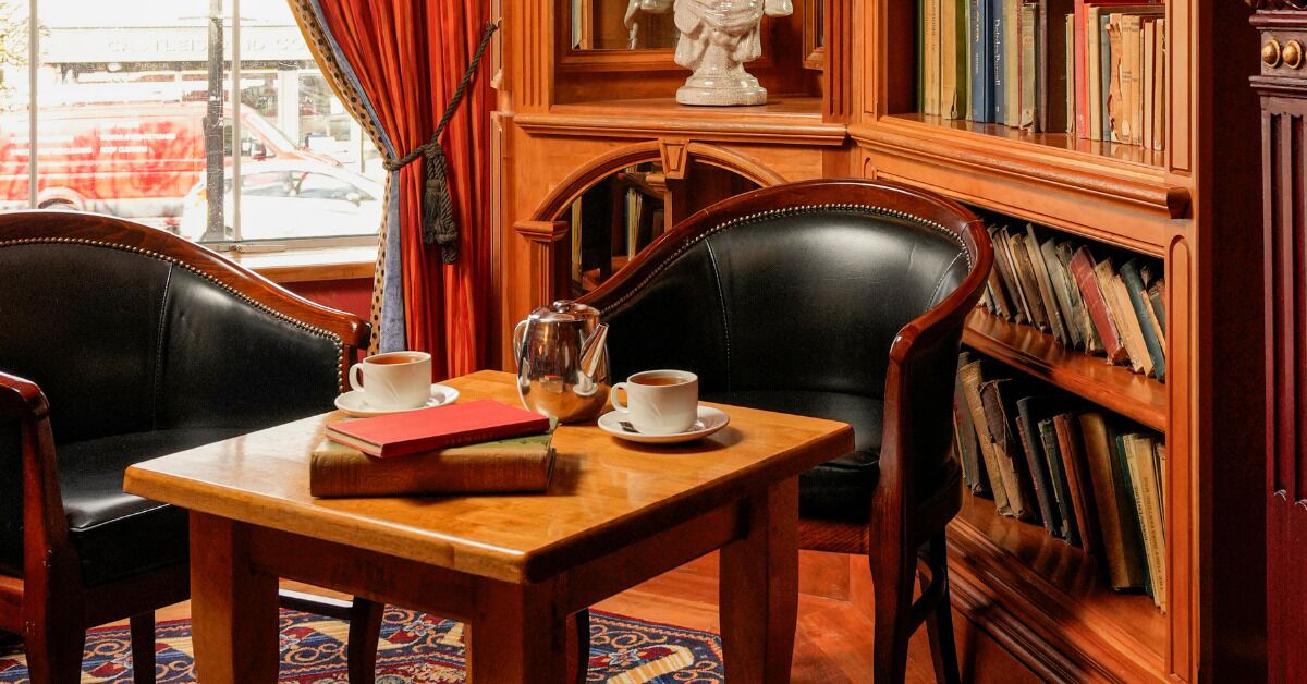 A wooden table with two chairs, a bookshelf with books, a statue, and a window with curtains.