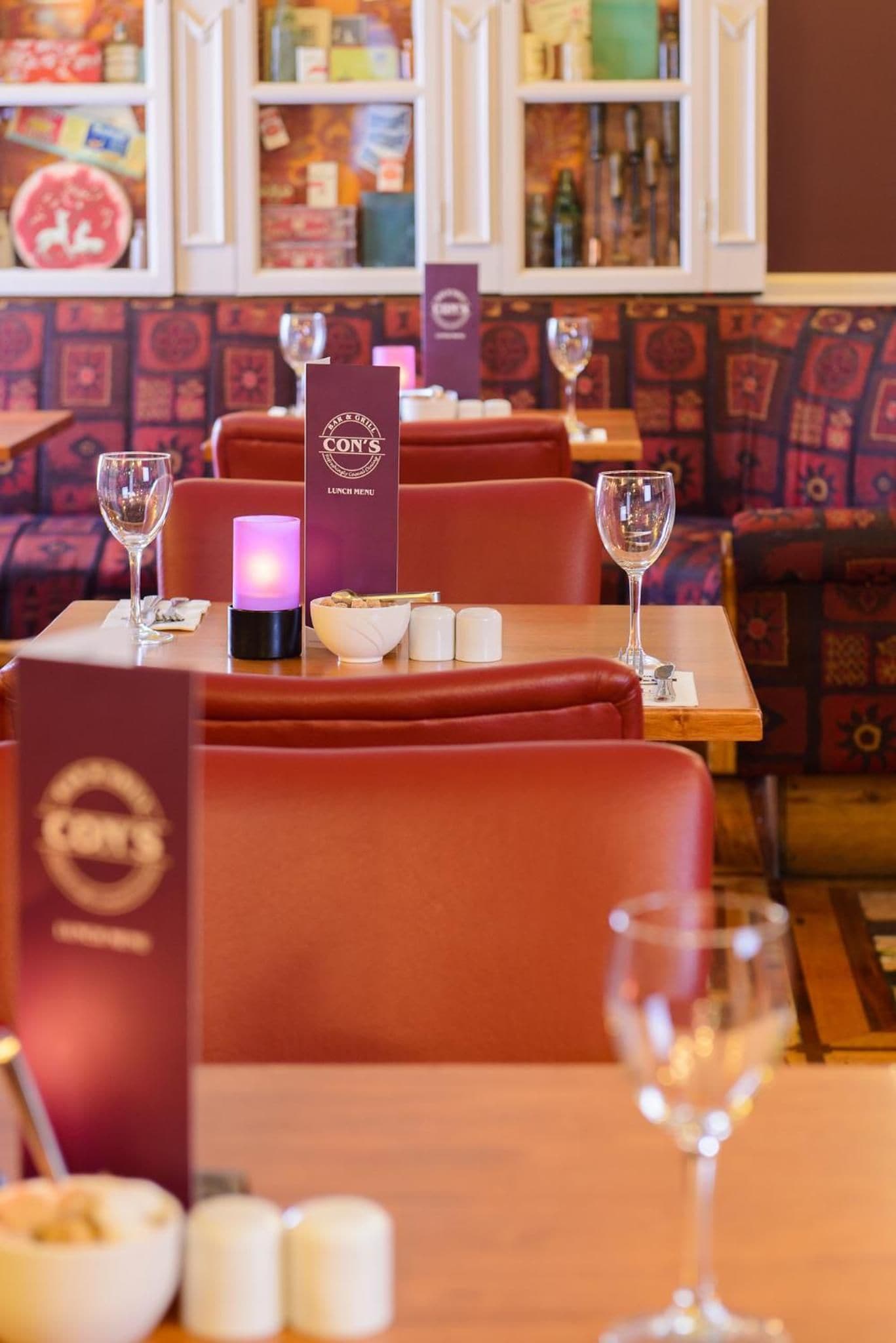 A restaurant interior with red booths, tables with wine glasses, and a menu stand.